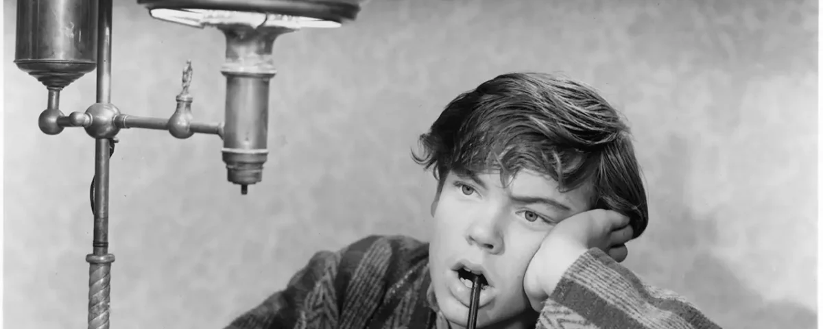 Image en noir et blanc de Bobby Driscoll, hypnotisé par une goutte d'eau d'un robinet d'évier, tenant une brosse à dents, appuyant sa tête sur sa main.