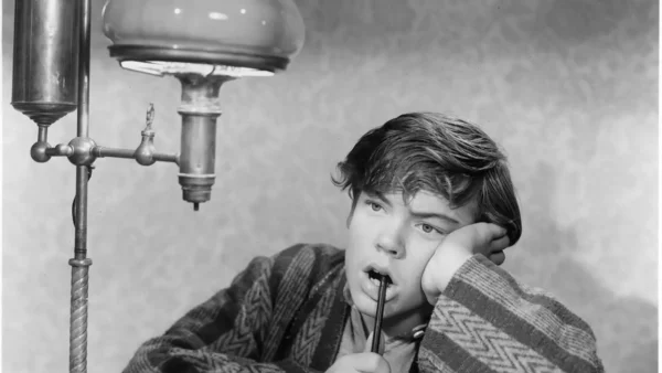 Image en noir et blanc de Bobby Driscoll, hypnotisé par une goutte d'eau d'un robinet d'évier, tenant une brosse à dents, appuyant sa tête sur sa main.