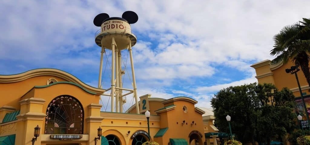 Entrée des studios Walt Disney présentant un grand château d'eau orné d'oreilles de Mickey Mouse sur un ciel bleu nuageux, encadré de bâtiments pastel jaunes et verts. Consultez les "horaires" pour connaître les heures d'ouverture