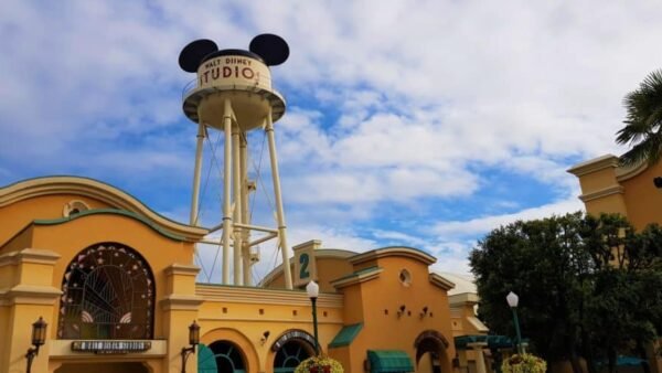 Entrée des studios Walt Disney présentant un grand château d'eau orné d'oreilles de Mickey Mouse sur un ciel bleu nuageux, encadré de bâtiments pastel jaunes et verts. Consultez les "horaires" pour connaître les heures d'ouverture
