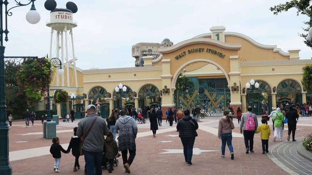 Les visiteurs, démontrant la forte fréquentation du parc, se dirigent vers l'entrée du Parc Walt Disney Studios, dotée d'une grande arcade portant le nom du parc et d'une statue de Mickey Mouse au sommet d'un