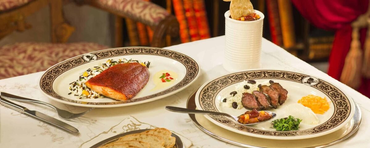 Un petit-déjeuner gastronomique servi sur une table élégamment dressée, composé d'une assiette de saucisses et d'œufs, d'un bol de yaourt aux fruits et d'un plat de saumon et d'œufs brouillés, entourés de formes