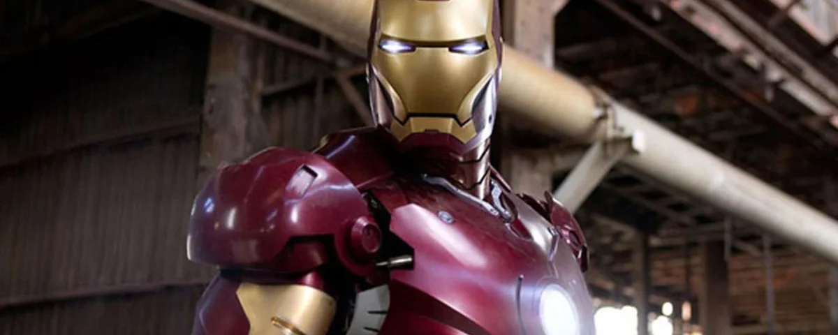 Iron Man en position de combat, vêtu de son costume emblématique rouge et or, dans un décor industriel avec poutres et tuyauterie visibles.