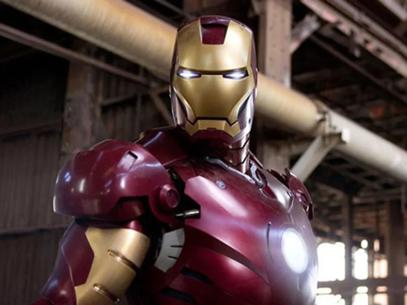 Iron Man en position de combat, vêtu de son costume emblématique rouge et or, dans un décor industriel avec poutres et tuyauterie visibles.