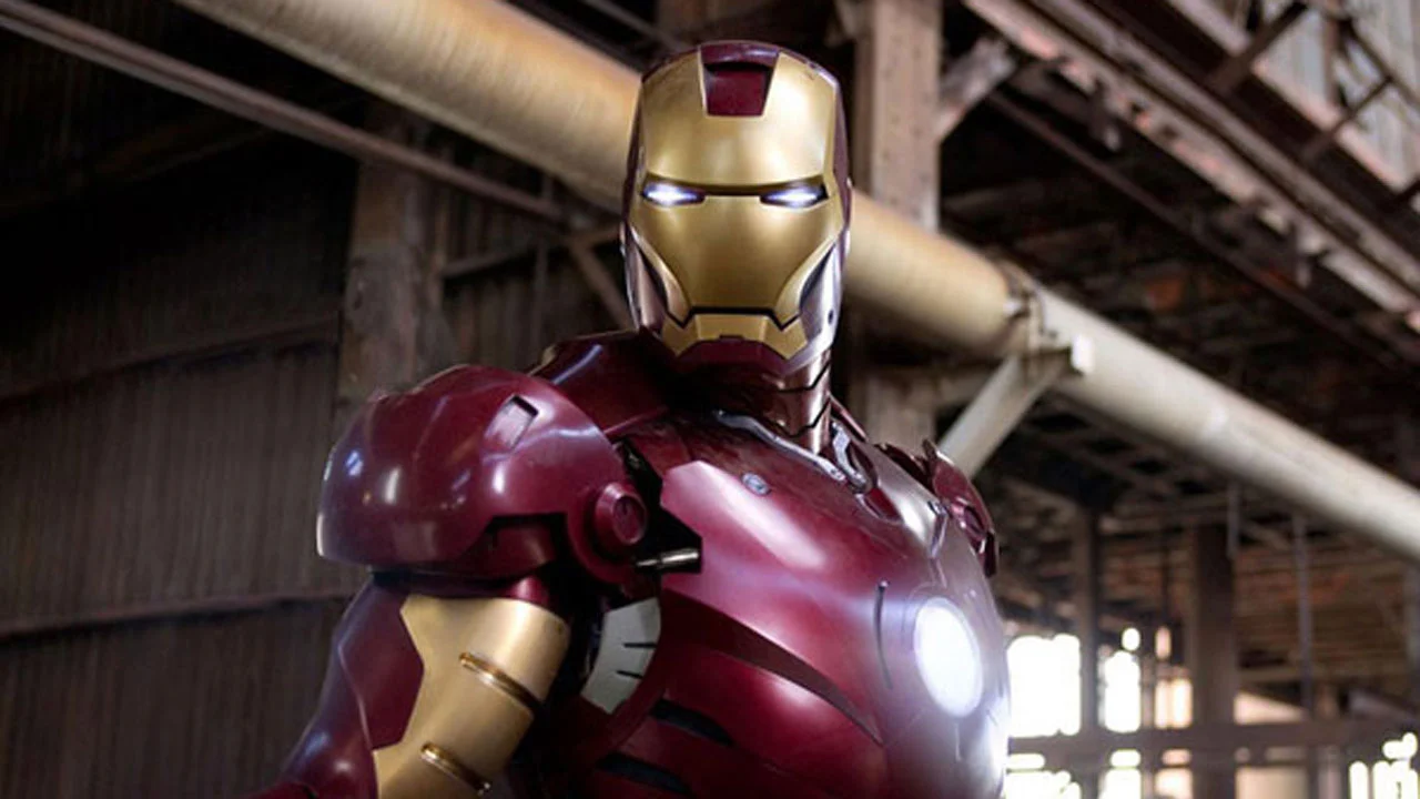 Iron Man en position de combat, vêtu de son costume emblématique rouge et or, dans un décor industriel avec poutres et tuyauterie visibles.