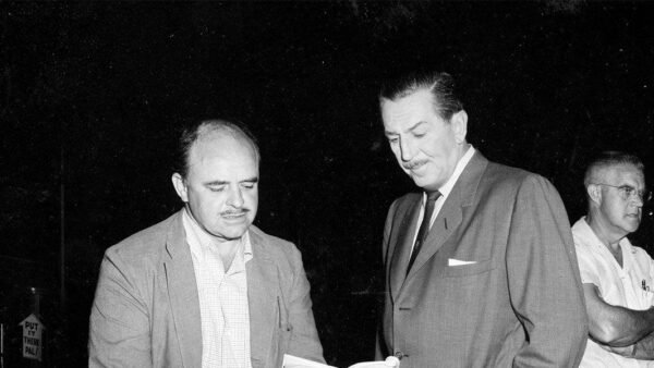 Deux hommes, l’un en costume et l’autre en veste décontractée et cravate, engagent une discussion sérieuse tout en regardant un document. Un homme plus âgé se tient à l'arrière-plan et observe la fusée rasta.
