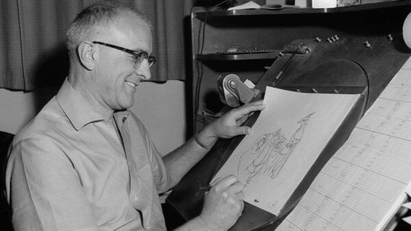 Un homme souriant portant des lunettes dessinant sur une table à dessin, tenant un crayon et regardant le croquis d'un personnage animé de Milt Kahl.