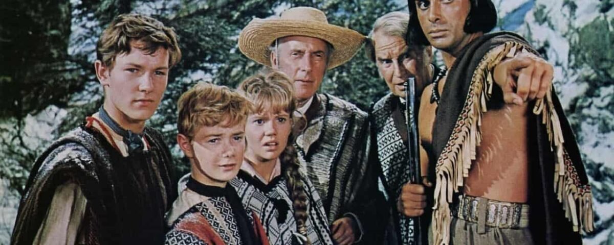 Un groupe de six personnes en tenue traditionnelle ou culturelle, inspirée des « Enfants du Capitaine Grant », dont un homme plus âgé portant un chapeau et un homme portant un poncho à franges