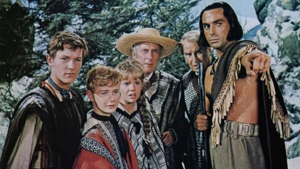Un groupe de six personnes en tenue traditionnelle ou culturelle, inspirée des « Enfants du Capitaine Grant », dont un homme plus âgé portant un chapeau et un homme portant un poncho à franges