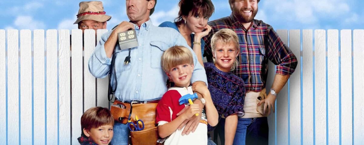 Casting de "Papa bricole" debout devant une clôture blanche, avec Tim Allen tenant des outils, rejoint par cinq autres membres du casting, affichant un mélange d'expressions ludiques et souriantes