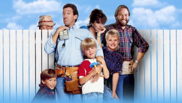 Casting de "Papa bricole" debout devant une clôture blanche, avec Tim Allen tenant des outils, rejoint par cinq autres membres du casting, affichant un mélange d'expressions ludiques et souriantes