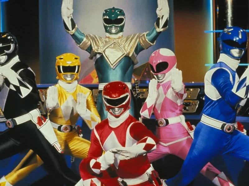 Cinq Power Rangers, vêtus de costumes éclatants (noir, vert, rose, rouge et bleu), prennent une pose triomphale ensemble dans un centre de commandement high-tech.