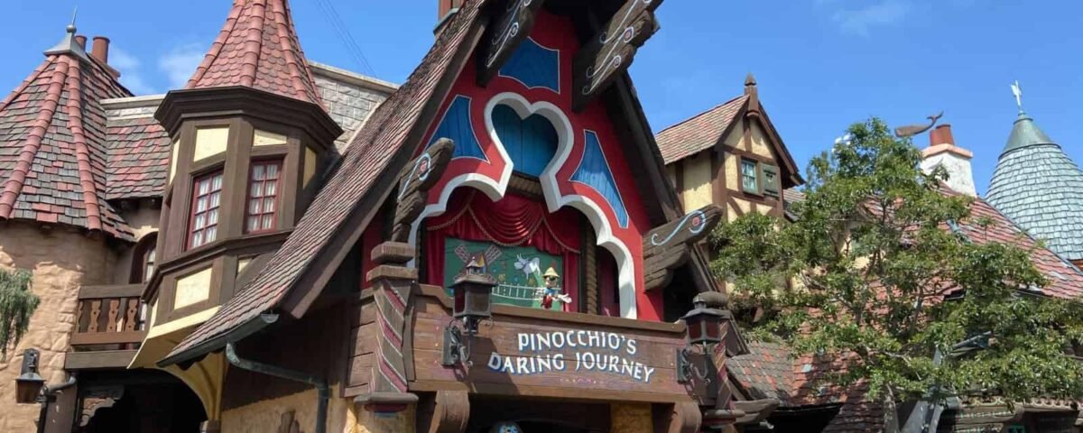 Vue extérieure du manège « Le voyage audacieux de Pinocchio » à Disneyland, avec une façade colorée de style livre de contes sous un ciel bleu clair.
