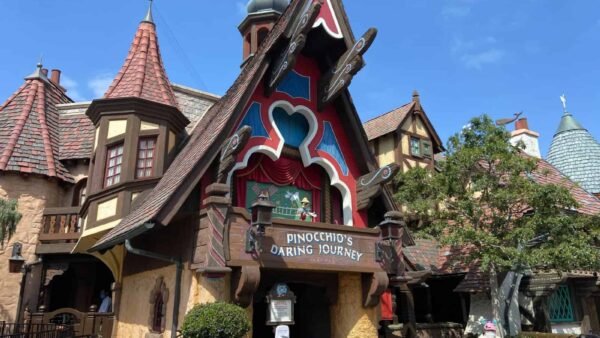 Vue extérieure du manège « Le voyage audacieux de Pinocchio » à Disneyland, avec une façade colorée de style livre de contes sous un ciel bleu clair.