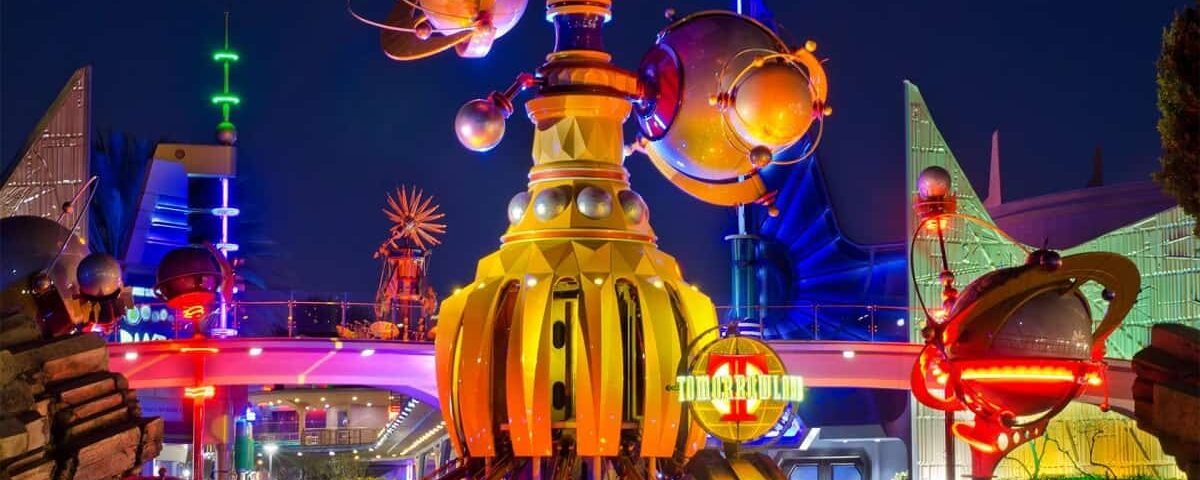 Une scène nocturne vibrante de Tomorrowland à Disneyland, avec des bâtiments futuristes avec des lumières brillantes et une structure dorée proéminente au premier plan.