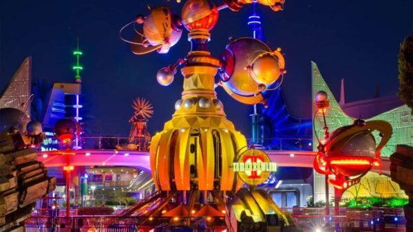 Une scène nocturne vibrante de Tomorrowland à Disneyland, avec des bâtiments futuristes avec des lumières brillantes et une structure dorée proéminente au premier plan.