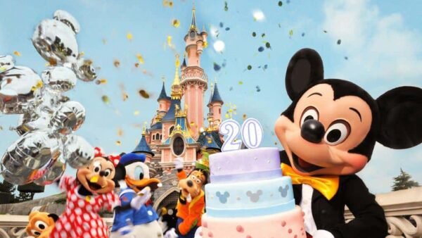 Mickey Mouse et ses amis font la fête avec un gâteau festif marqué "20" devant le château de Disneyland Paris, avec des confettis et des ballons dans les airs.