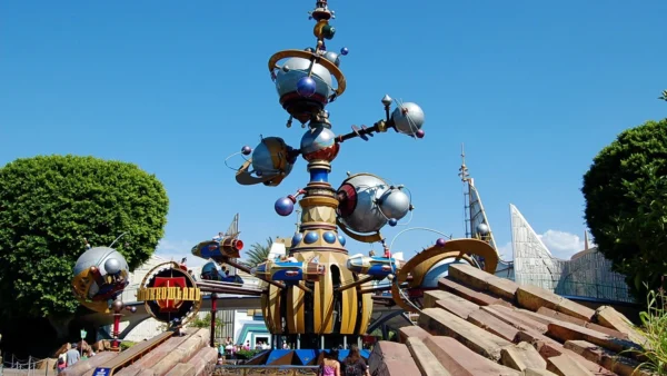 Une sculpture imaginative et futuriste ressemblant à l'Astro Orbiter dans un parc à thème, avec des couleurs vives, des éléments sphériques et des détails mécaniques sous un ciel bleu clair.