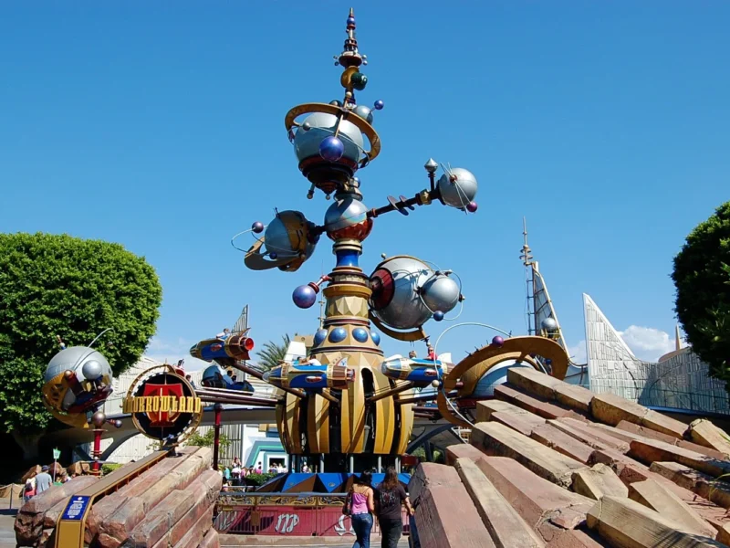 Une sculpture imaginative et futuriste ressemblant à l'Astro Orbiter dans un parc à thème, avec des couleurs vives, des éléments sphériques et des détails mécaniques sous un ciel bleu clair.