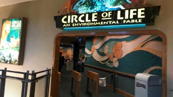 Entrée de l'attraction « Cercle de la vie : une fable environnementale », comprenant une enseigne lumineuse avec des personnages de films et une fresque murale représentant les vagues de l'océan à côté d'un portail ouvert.
