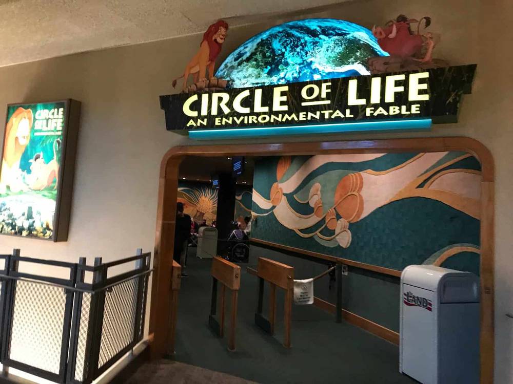 Entrée de l'attraction « Cercle de la vie : une fable environnementale », comprenant une enseigne lumineuse avec des personnages de films et une fresque murale représentant les vagues de l'océan à côté d'un portail ouvert.