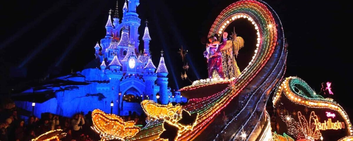 Un défilé nocturne animé à Disneyland mettant en vedette le char Fantillusion avec une arche arc-en-ciel et des personnages en costumes colorés, avec le château de Cendrillon illuminé en arrière-plan.