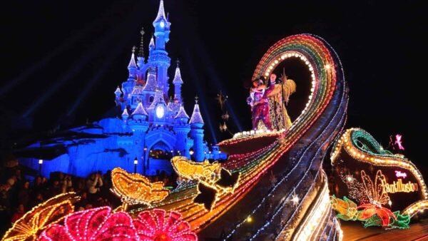 Un défilé nocturne animé à Disneyland mettant en vedette le char Fantillusion avec une arche arc-en-ciel et des personnages en costumes colorés, avec le château de Cendrillon illuminé en arrière-plan.