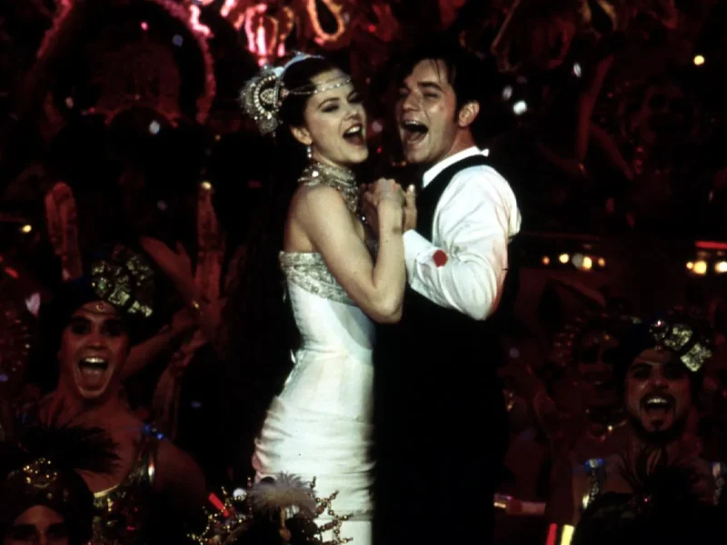 Une scène joyeuse mettant en scène une femme en robe blanche et un homme en smoking dansant en étroite collaboration parmi un groupe d'artistes excités aux costumes vibrants au Moulin Rouge.