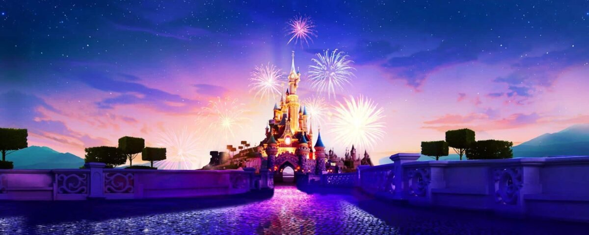Des feux d'artifice illuminent le ciel au-dessus de Disneyland Paris au crépuscule, avec un reflet scintillant dans l'eau des douves environnantes.