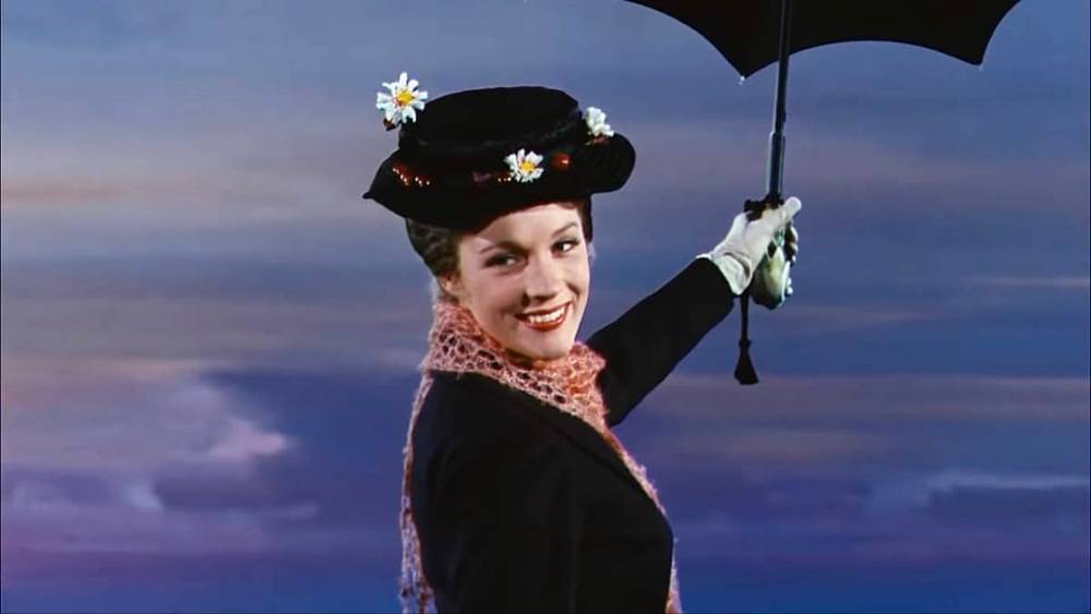 Une femme en tenue vintage sourit, tenant un parapluie noir. Inspirée de Mary Poppins, elle porte un chapeau à bords orné de fleurs et une écharpe en dentelle, sur un ciel crépusculaire.