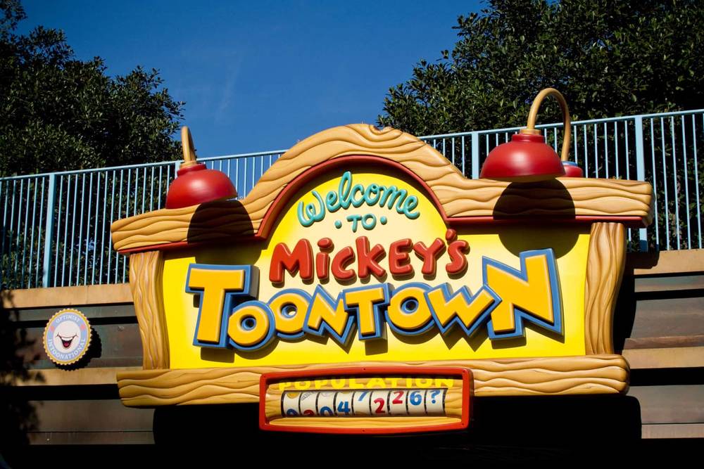 Un panneau vibrant à l'entrée de Mickey's Toontown à Walt Disney World avec des polices audacieuses et fantaisistes, avec des lampes rouges décoratives en haut et un compteur de population en bas.