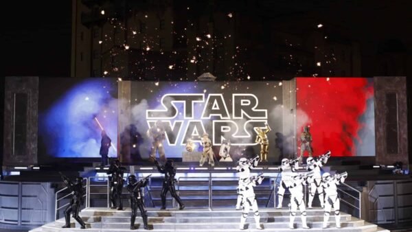 Un spectacle de festival vibrant mettant en vedette des personnages en costumes, notamment des stormtroopers et des pirates, sous une pancarte étincelante. Des fonds bleus et rouges complètent la scène.