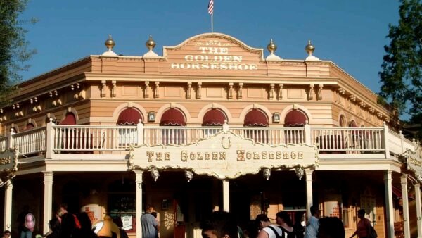 Vue frontale du bâtiment Golden Horseshoe Revue dans un parc d'attractions par une journée ensoleillée, avec une façade de deux étages de style occidental avec des gens marchant devant.