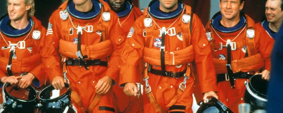 Un groupe de six astronautes vêtus de combinaisons et de casques orange vif, marchant en toute confiance avec en toile de fond un grand drapeau américain, prêts pour une mission Armageddon.