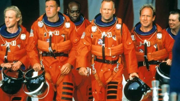 Un groupe de six astronautes vêtus de combinaisons et de casques orange vif, marchant en toute confiance avec en toile de fond un grand drapeau américain, prêts pour une mission Armageddon.