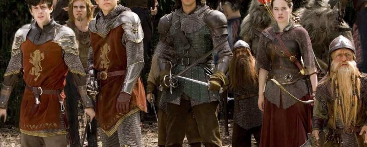 Un groupe d'acteurs vêtus d'armures et de costumes de style médiéval, debout dans un décor forestier, se faisant passer pour des personnages d'un film fantastique. Certains brandissent des épées et arborent des emblèmes distinctifs sur leurs tenues, notamment un