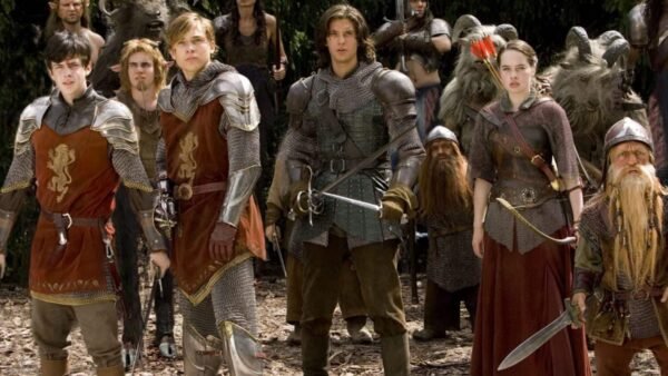 Un groupe d'acteurs vêtus d'armures et de costumes de style médiéval, debout dans un décor forestier, se faisant passer pour des personnages d'un film fantastique. Certains brandissent des épées et arborent des emblèmes distinctifs sur leurs tenues, notamment un