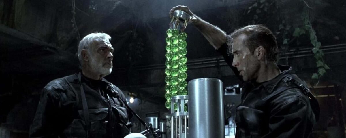 Deux hommes, dont The Rock, examinent un appareil cylindrique futuriste rempli de sphères vertes brillantes dans un cadre industriel faiblement éclairé.