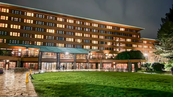 Vue nocturne d'un grand bâtiment moderne de Disneyland Paris, éclairé par un éclairage chaleureux, comprenant plusieurs étages avec de grandes fenêtres en verre et une pelouse bien entretenue au premier plan.