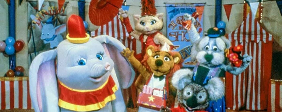 Une scène colorée mettant en scène des personnages animaux anthropomorphes dans le chapiteau de cirque de Dumbo : un éléphant, un écureuil, une souris et un koala, tous vêtus d'une tenue de cirque ludique.
