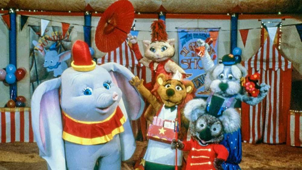 Une scène colorée mettant en scène des personnages animaux anthropomorphes dans le chapiteau de cirque de Dumbo : un éléphant, un écureuil, une souris et un koala, tous vêtus d'une tenue de cirque ludique.