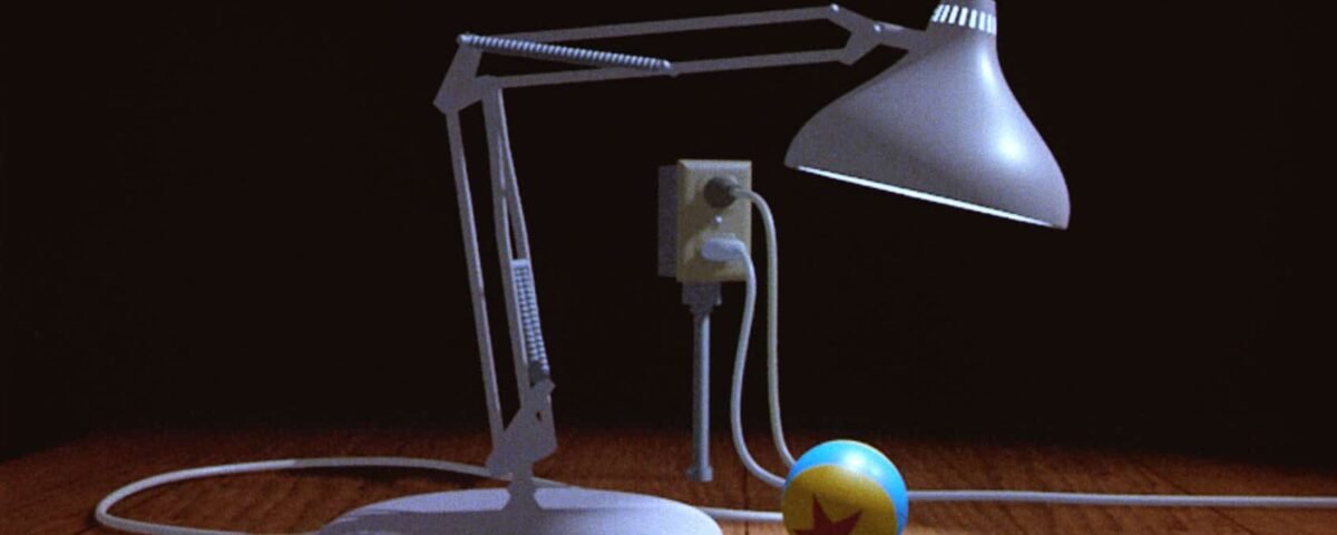 Une lampe Luxo animée se penche pour regarder une petite boule avec une étoile dessus, posée sur une surface texturée en bois dans une pièce faiblement éclairée.