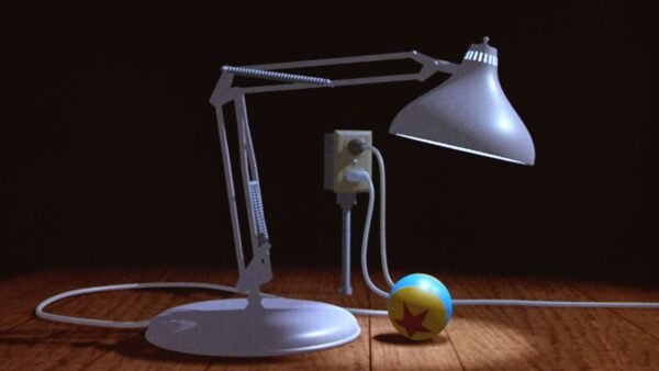 Une lampe Luxo animée se penche pour regarder une petite boule avec une étoile dessus, posée sur une surface texturée en bois dans une pièce faiblement éclairée.
