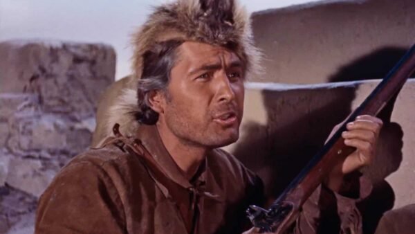 Un homme en costume historique de Davy Crockett, portant un chapeau de fourrure, lève les yeux avec inquiétude tout en tenant un fusil, sur fond de pierre.
