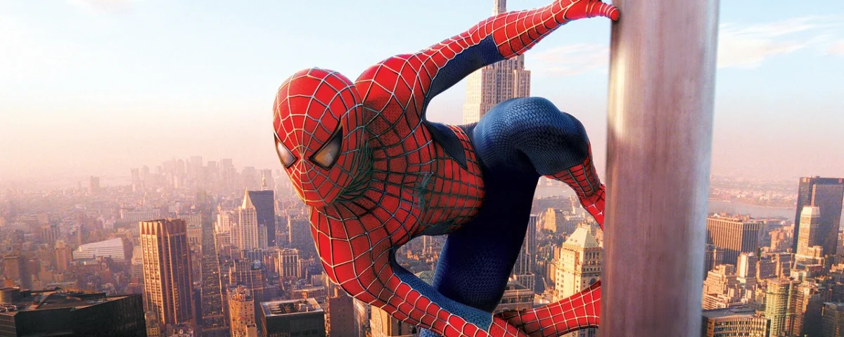 Spiderman, dans son emblématique costume rouge et bleu, escalade un gratte-ciel avec un paysage urbain animé et un ciel dégagé en arrière-plan.