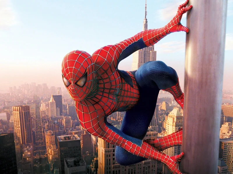 Spiderman, dans son emblématique costume rouge et bleu, escalade un gratte-ciel avec un paysage urbain animé et un ciel dégagé en arrière-plan.
