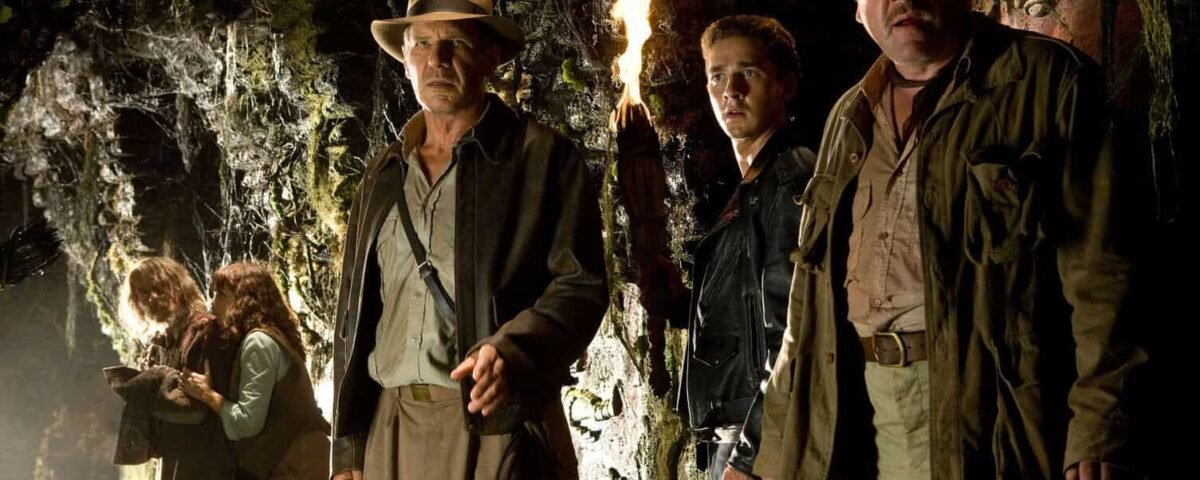 Trois hommes en tenue d'aventure se tiennent dans une grotte faiblement éclairée, tenant des torches, entourés de murs de pierre recouverts d'anciens glyphes, affichant des expressions de curiosité et d'appréhension alors qu'ils se préparent à entrer dans demain.