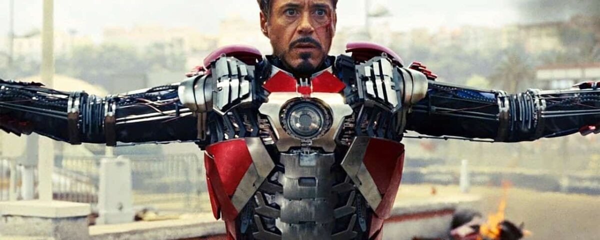 Tony Stark dans sa combinaison Iron Man 2, les bras tendus, montrant les détails mécaniques et la technologie de la combinaison sur un fond urbain flou.
