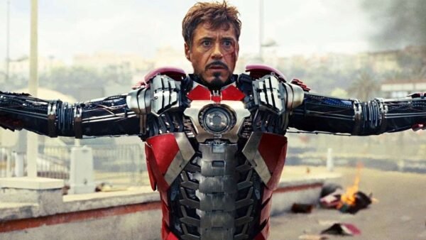 Tony Stark dans sa combinaison Iron Man 2, les bras tendus, montrant les détails mécaniques et la technologie de la combinaison sur un fond urbain flou.