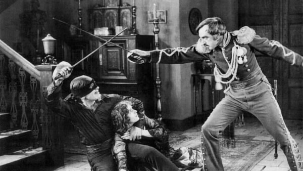 Un film en noir et blanc représentant une scène dramatique de combat à l'épée entre deux hommes en costumes ornés, avec une femme en détresse accroupie sur Main Street en arrière-plan.